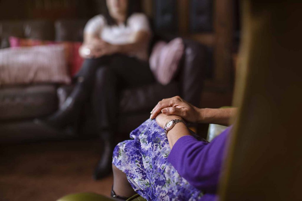 cardinal-therapist-hands-resting-lap Seated Cardinal Clinic therapist with their hands resting on their knee during therapy session